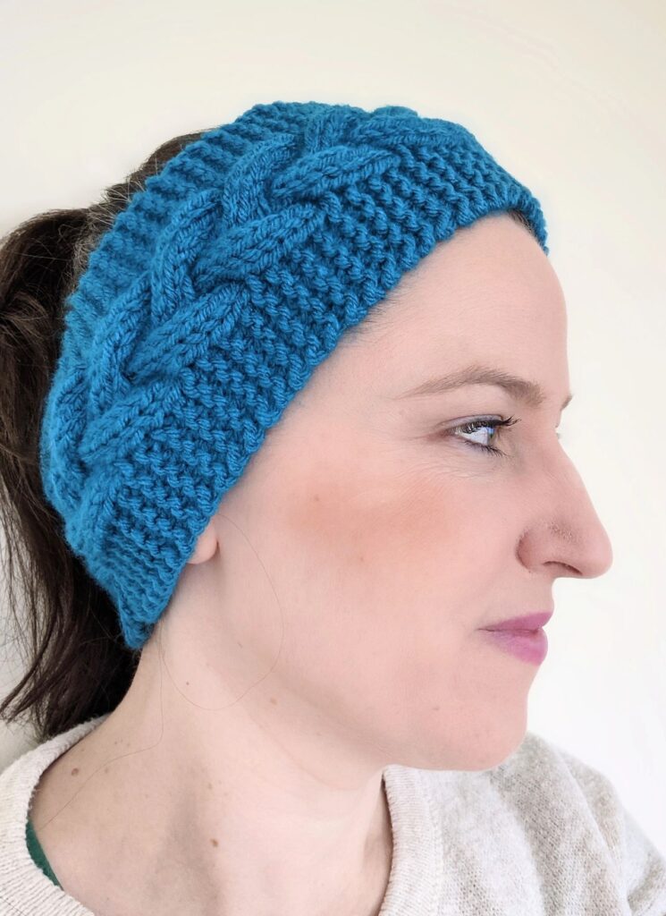 This is Megan looking to the side and wearing an emerald colour knitted headband, which features a knitted cable section in the centre